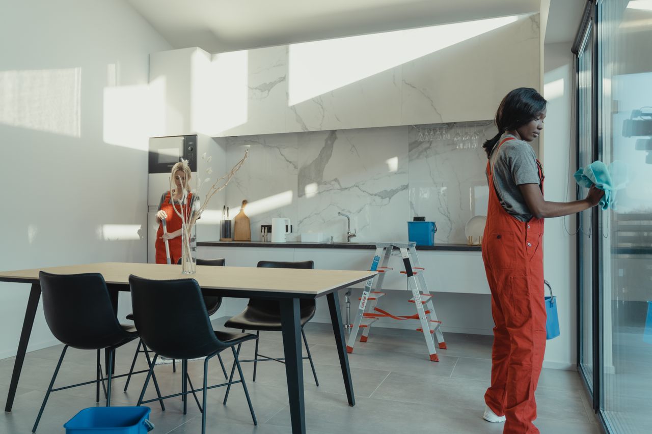 why-choose-us Two women in work clothes cleaning a kitchen with glass doors.
